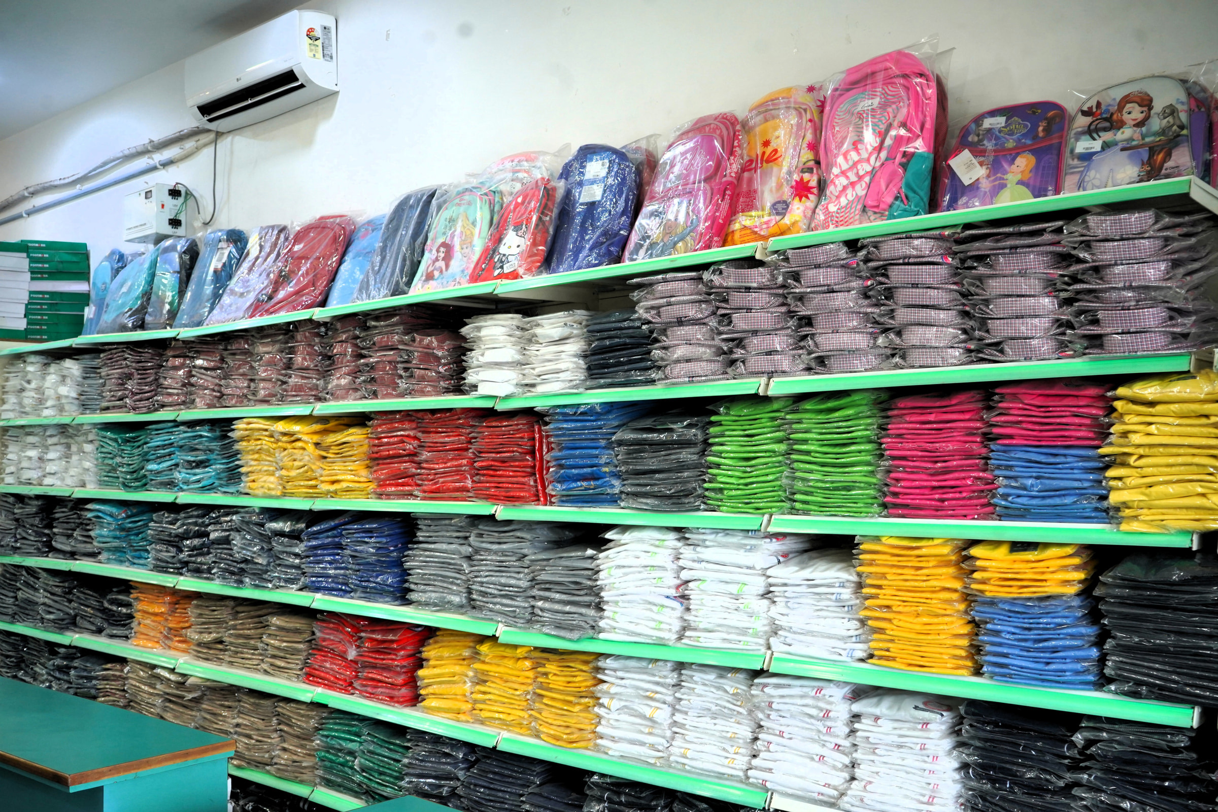 School bags along the top shelf at Kharar, shirts stacked beneath